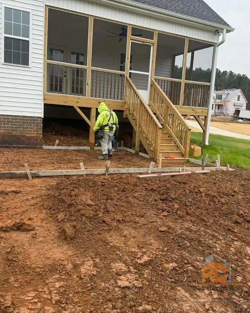 Crew member finishing a fresh concrete slab beside a covered porch
